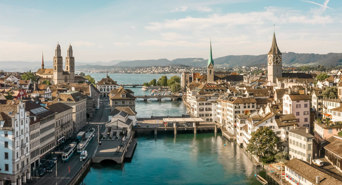 Panoramablick auf Zürich mit der Limmat, historischen Gebäuden, Kirchtürmen und dem Zürichsee im Hintergrund.