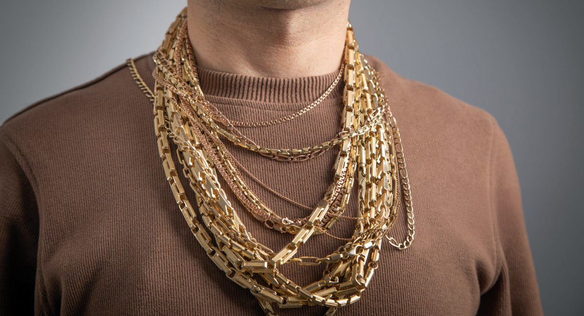 Ein Nackenausschnitt eines Mannes, der einen braunen Pullover und mehrere Goldketten trägt.